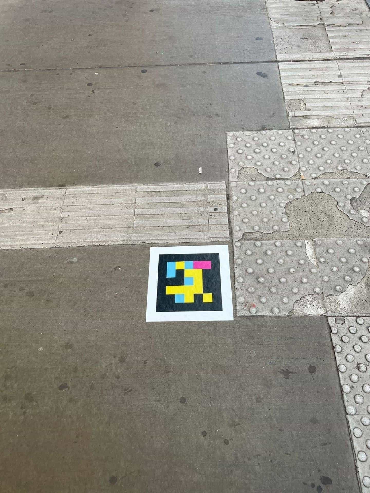 Concrete paving in front of the Hbf with tactile slabs and channeling strips; in the centre, a square NaviLens code stuck to the floor