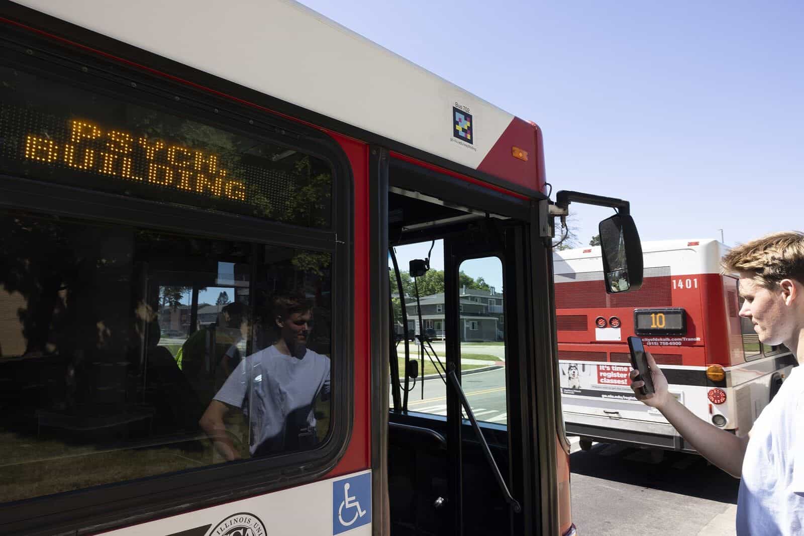 Student pointing their mobile phone at a NaviLens code (Bus 702 go.niu.edu/wayfinding) installed on the door of a DeKalb city bus