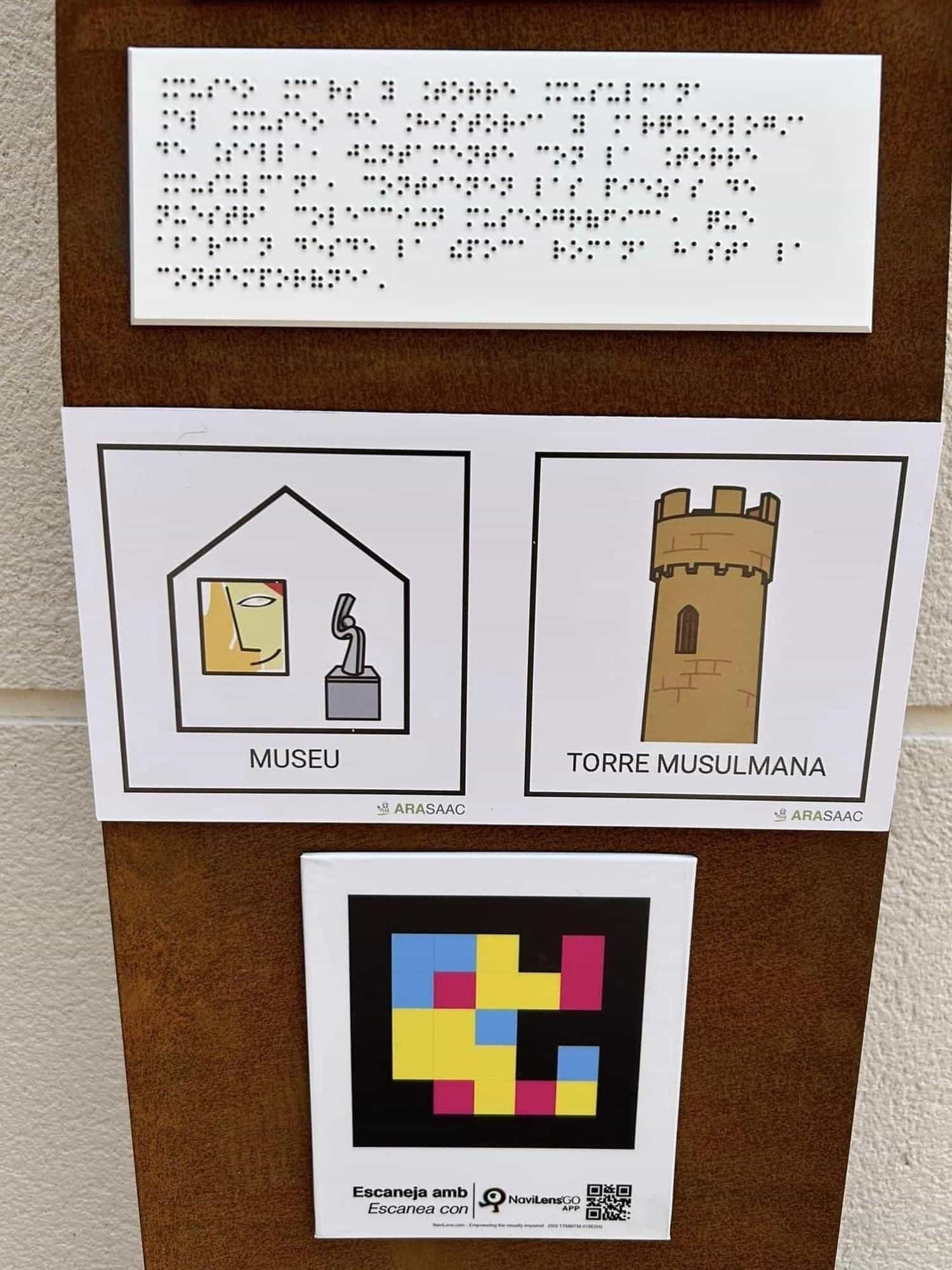 Top detail of a Silla totem: braille plate, two ARASAAC pictograms “MUSEU” and “TORRE MUSULMANA”, and NaviLens code with “Escaneja amb / Escanea con NaviLens GO APP” and an extra QR.