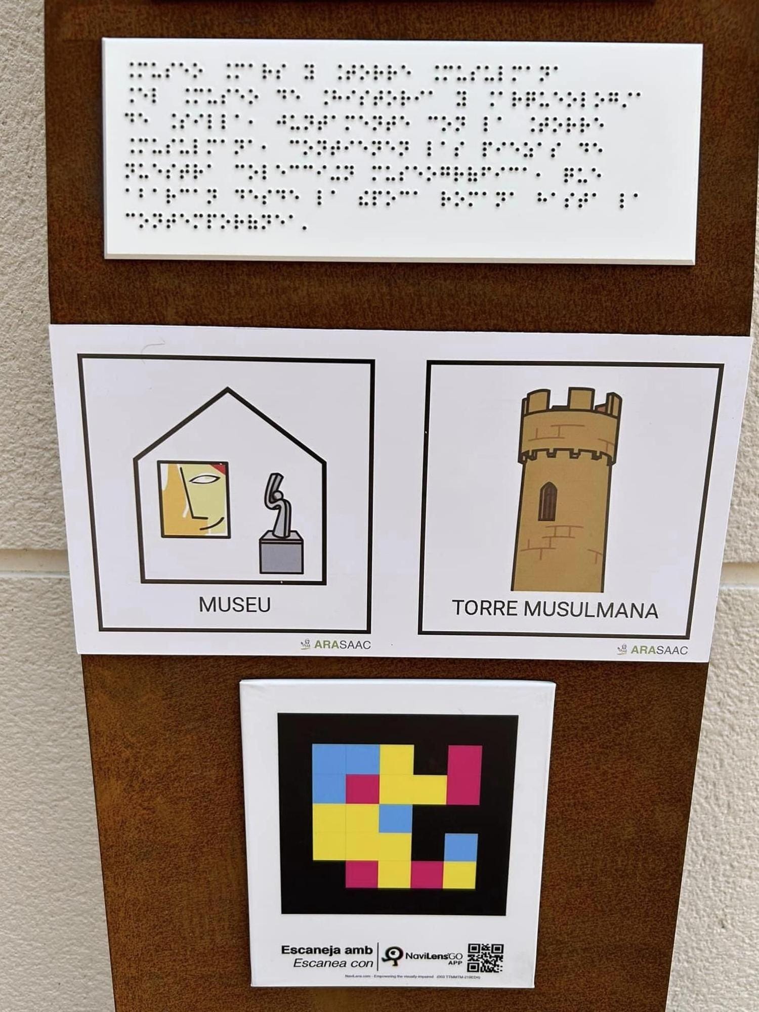 Top detail of a Silla totem: braille plate, two ARASAAC pictograms “MUSEU” and “TORRE MUSULMANA”, and NaviLens code with “Escaneja amb / Escanea con NaviLens GO APP” and an extra QR.