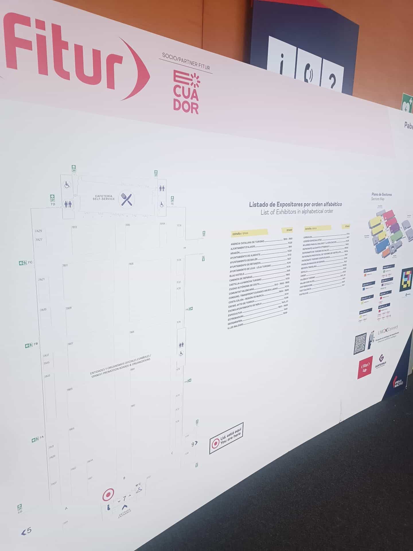 Direttorio del Padiglione 7 di IFEMA MADRID con la pianta del padiglione a sinistra, l’elenco alfabetico degli espositori al centro e, a destra, la pianta dei settori accanto a un cartello dello stesso FITUR 4all con il suo codice NaviLens