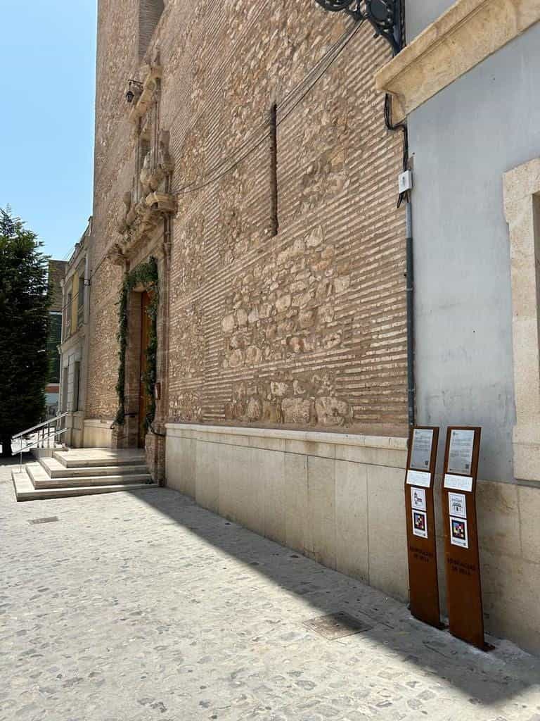 Calle empedrada de Silla con dos tótems de acero corten alineados junto al lateral de la Iglesia de la Virgen de los Ángeles.