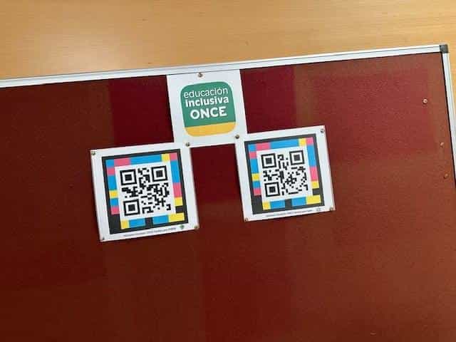 Red cork noticeboard with two framed square colour NaviLens codes and, between them, the “Educación inclusiva ONCE” seal on a green and yellow background
