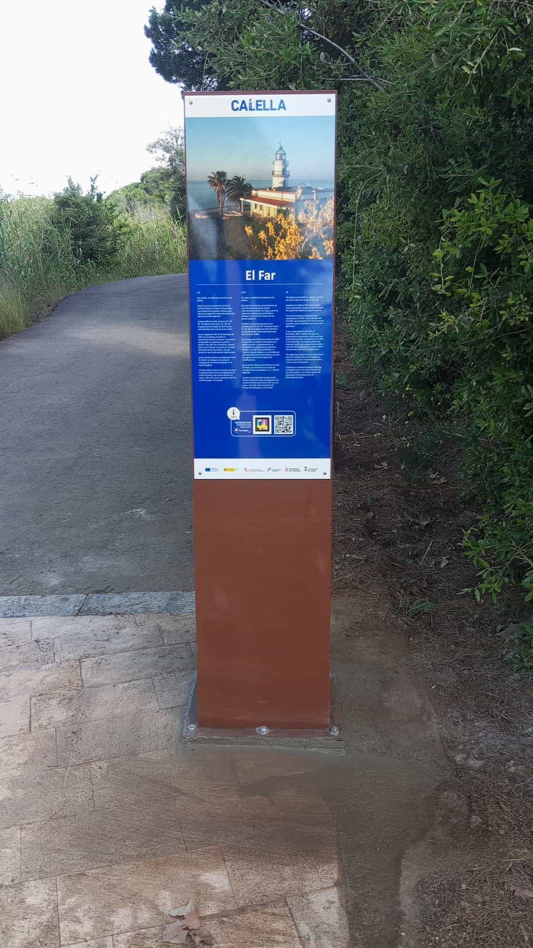 Tótem CALELLA de El Far, con foto del faro y código NaviLens, junto al camino de acceso al faro de Calella