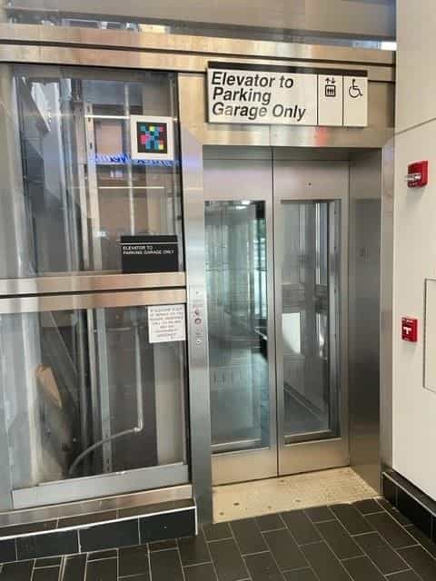 «Elevator to Parking Garage Only» with a NaviLens code high on the glass partition and a printed service notice on the side panel
