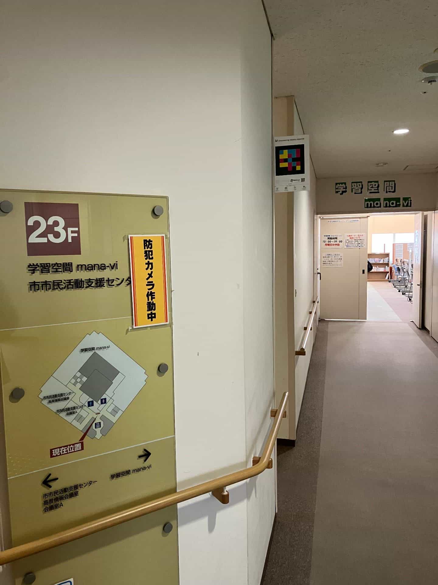 Accès au 23ᵉ étage du Yamagata City Civic Activity Support Center avec le panneau 学習空間 mana-vi et un code NaviLens sur la colonne du couloir