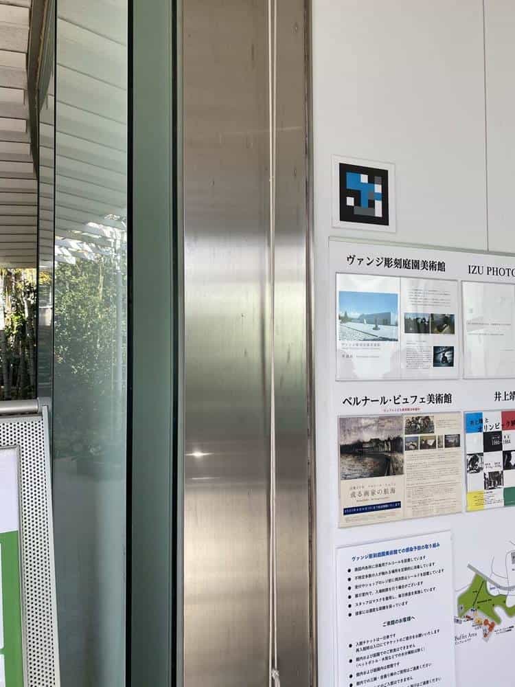Entrance of the Vangi Sculpture Garden Museum (Clematis no Oka, Shizuoka) with a cyan, magenta and yellow NaviLens code stuck on a metal post next to the venue's information panel