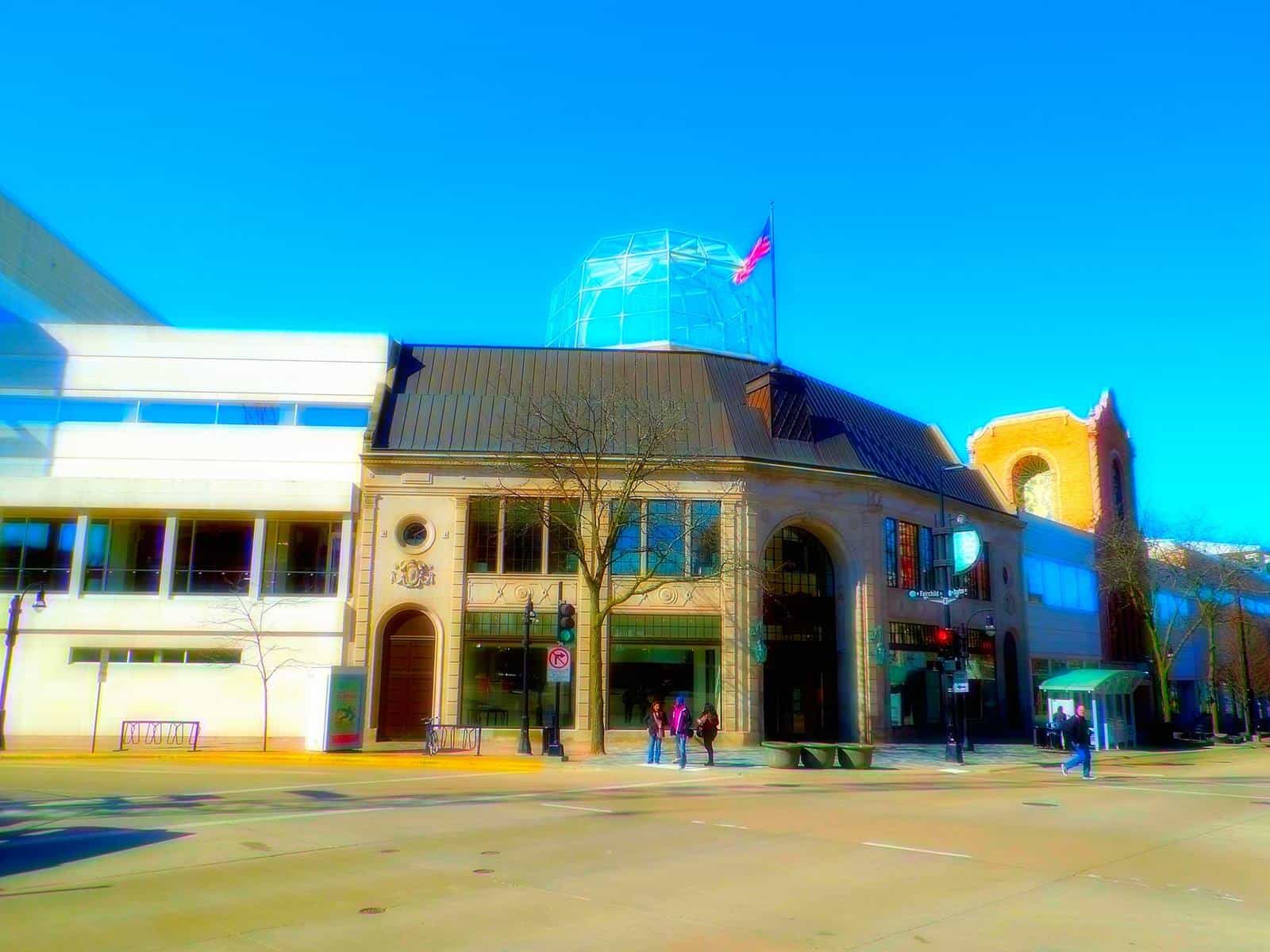 Main entrance of Overture Center on State Street, Madison: light stone facade with an arched entry, a glass dome on the roof and the brick tower of the former Capitol Theater on the right