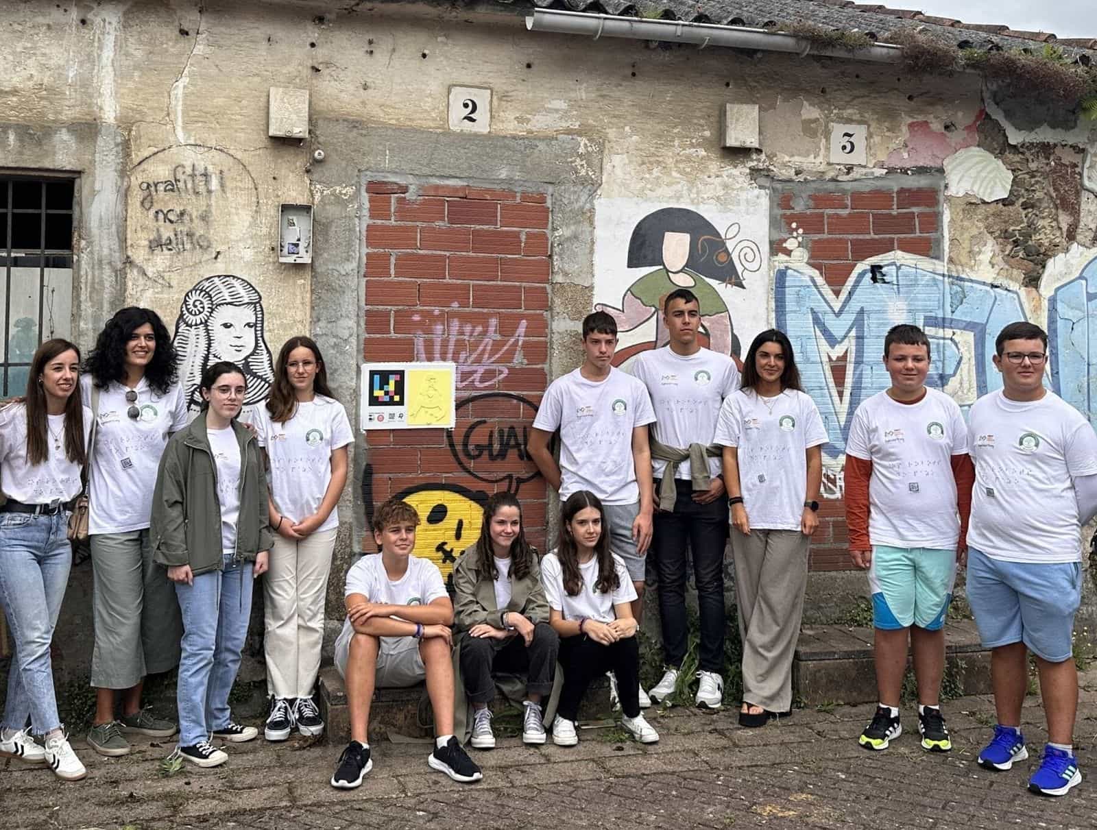 Foto di gruppo di Os Robots do Pazo (IES de Fene) con le loro insegnanti davanti a un pannello «Tocando as Meninas» installato su una facciata di Canido accanto a un murale della Menina con la cuffia