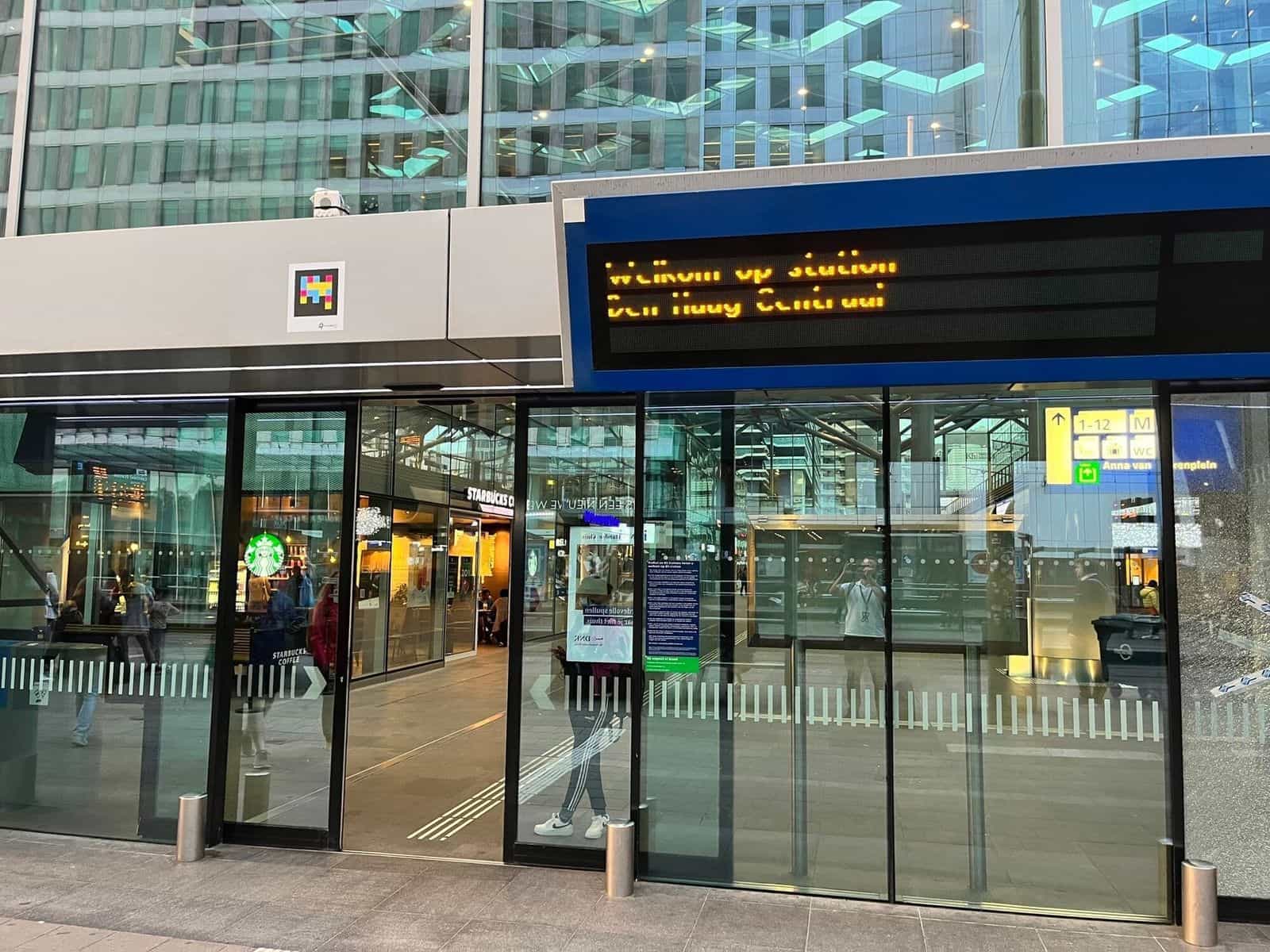 Banchina esterna di tram/autobus accanto a Den Haag Centraal al tramonto, con linea guida tattile scanalata e un codice NaviLens applicato al pavimento alla fine della linea