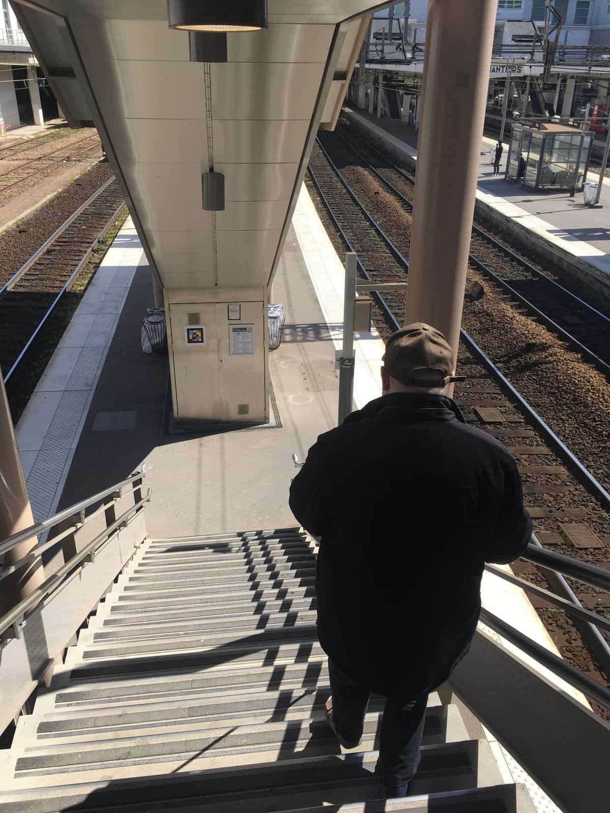 Passenger going down the metal stairs to the platform, NaviLens code on technical cabinet.