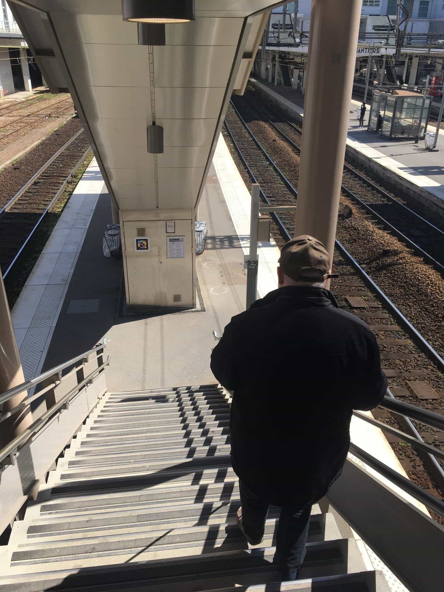 Passenger going down the metal stairs to the platform, NaviLens code on technical cabinet.