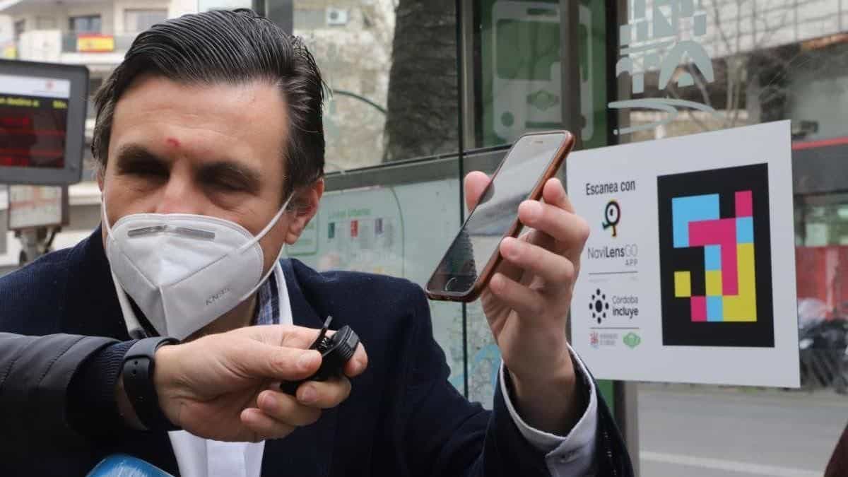 Persona escaneando con un iPhone el cartel «Escanea con NaviLens GO · Córdoba Incluye» en una marquesina de AUCORSA