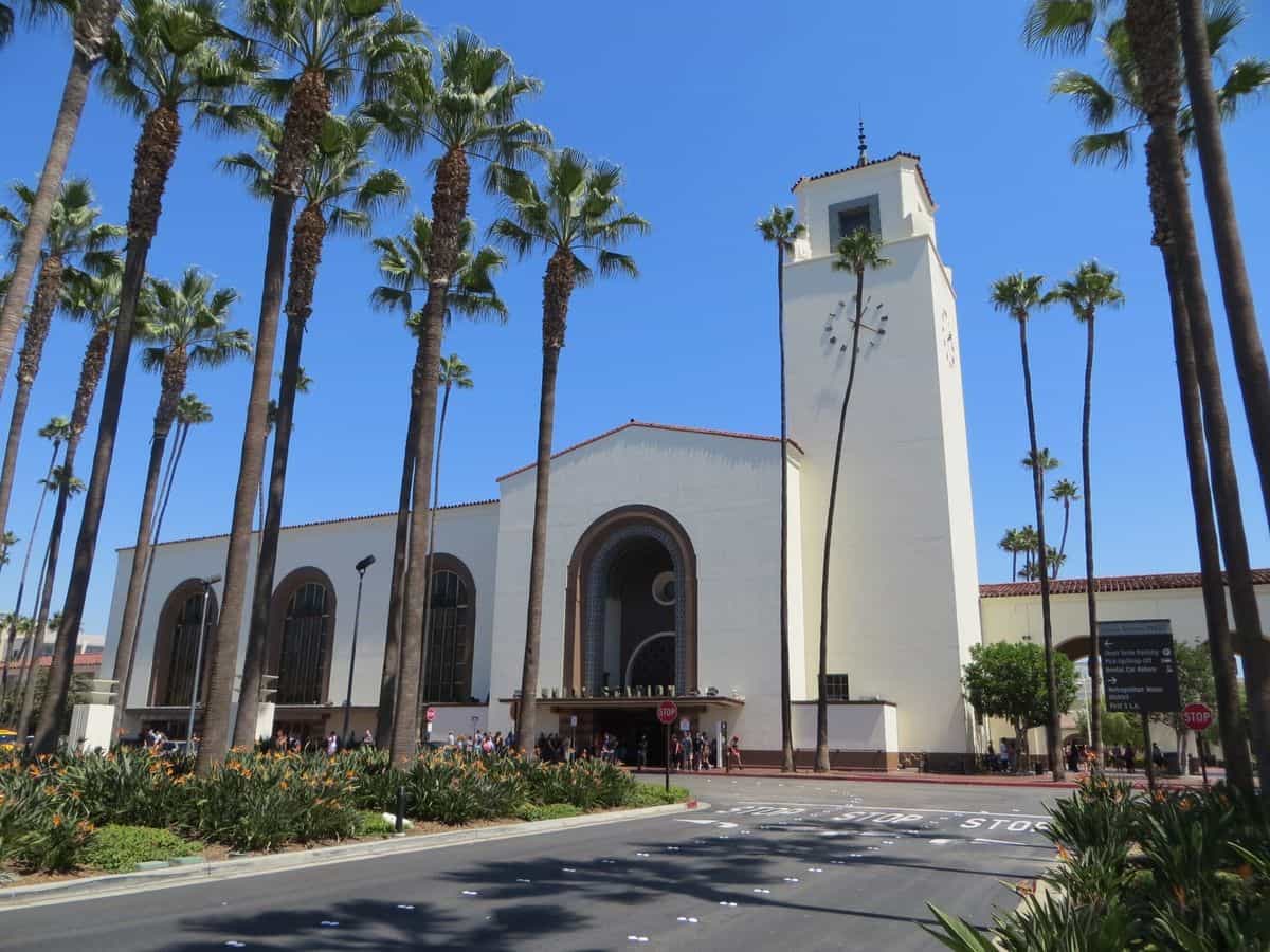 Vista frontal del edificio principal de Union Station: arquitectura Mission Revival y Streamline Moderne con torre del reloj, palmeras altas y entrada peatonal al vestíbulo histórico