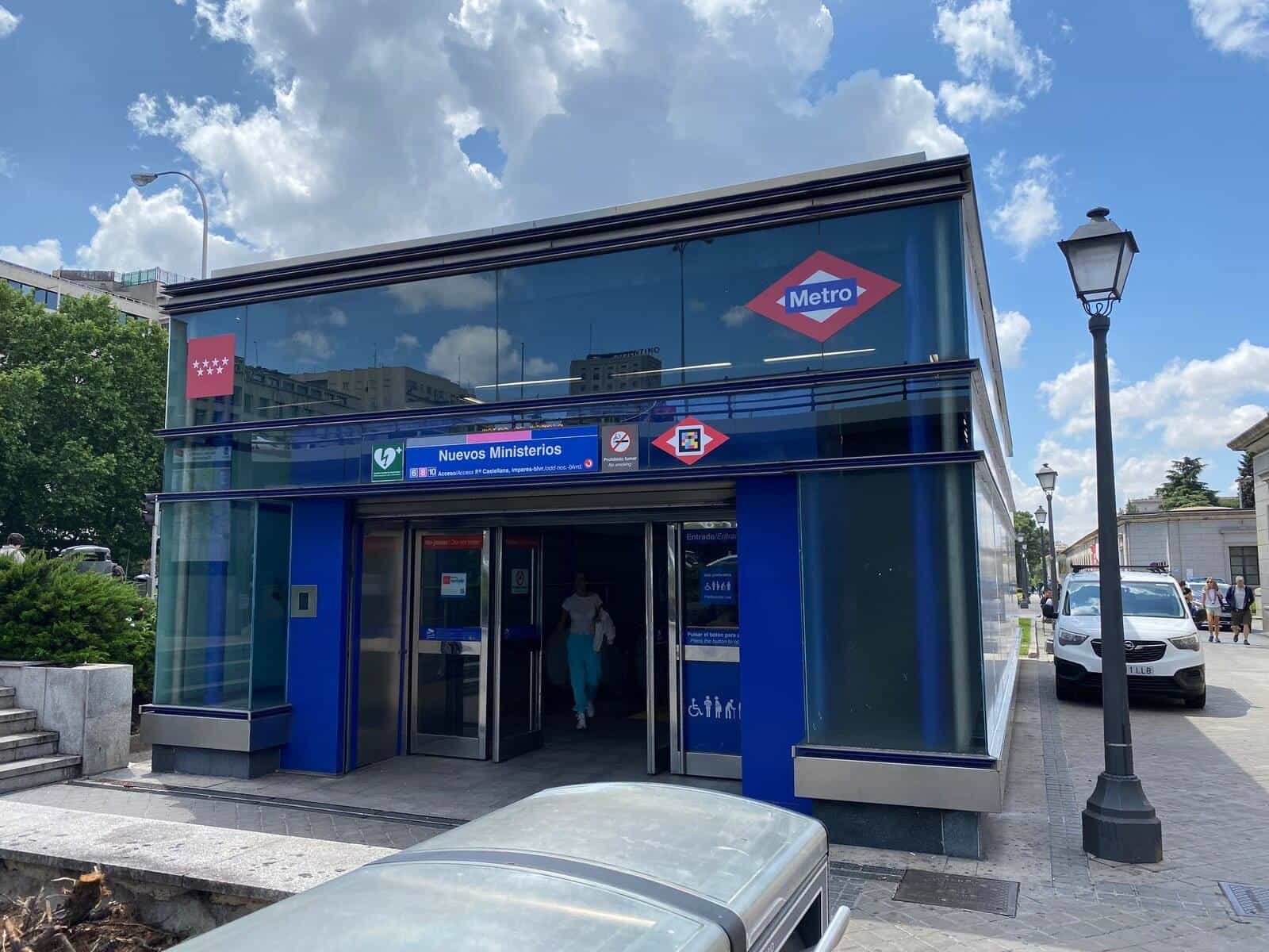 Another outdoor access to Nuevos Ministerios from Paseo de la Castellana: identical glass cube with the Community of Madrid flag, Metro red diamond and “Nuevos Ministerios” sign with the icons of lines 6, 8 and 10 and NaviLens code