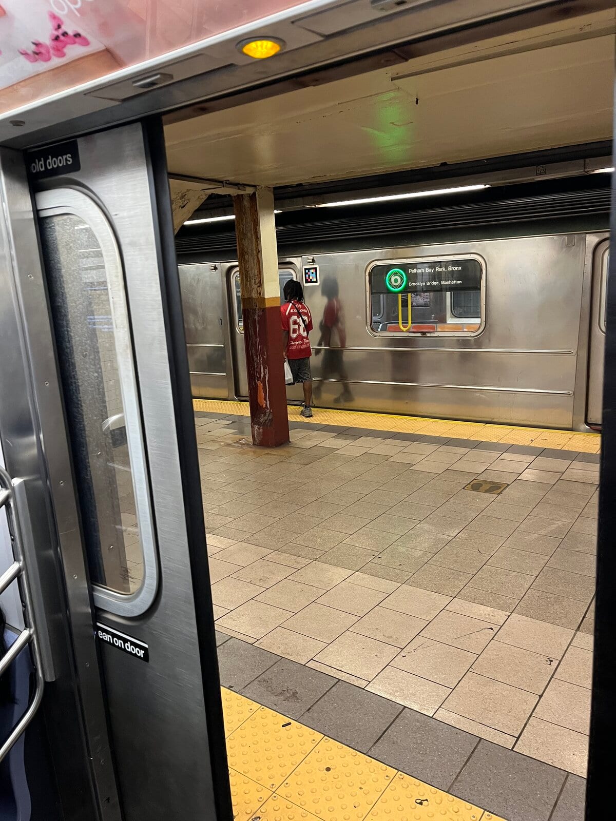 Voiture de la ligne 6 dans une station du métro de New York ; sur la face avant, le panneau lumineux «Pelham Bay Park, Bronx / Brooklyn Bridge, Manhattan» et, près de la fenêtre, un marqueur coloré NaviLens