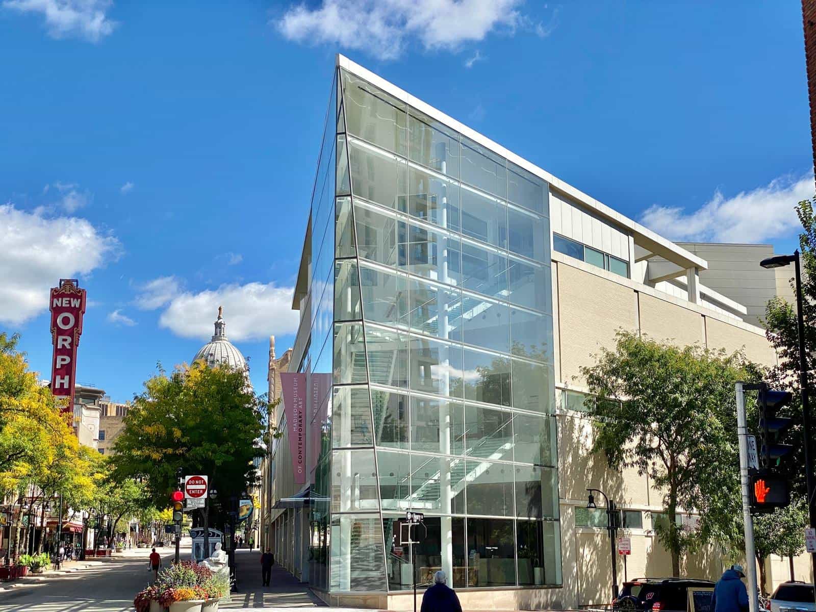 Glass facade of Overture Center at the corner of State Street and Henry Street, Madison: the glass box of the Madison Museum of Contemporary Art with its interior staircase, the Wisconsin State Capitol dome in the background and the vertical New Orpheum sign on the left