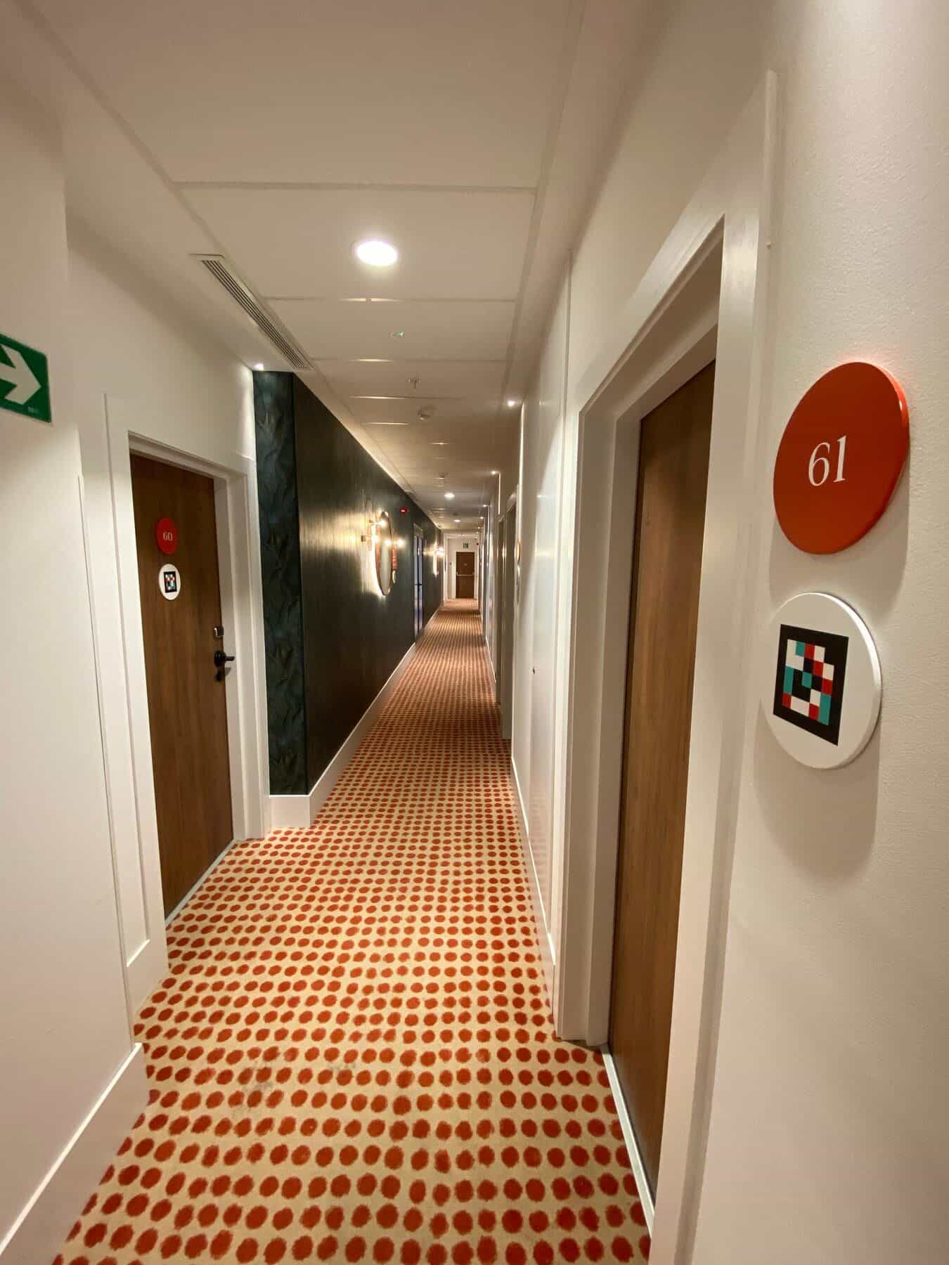 Fassade des ibis Styles Sevilla City Santa Justa: großes weißes Betongebäude mit quadratischen Fenstern und einem zentralen roten Bogenkörper, gekrönt vom grünen „ibis styles“-Schriftzug