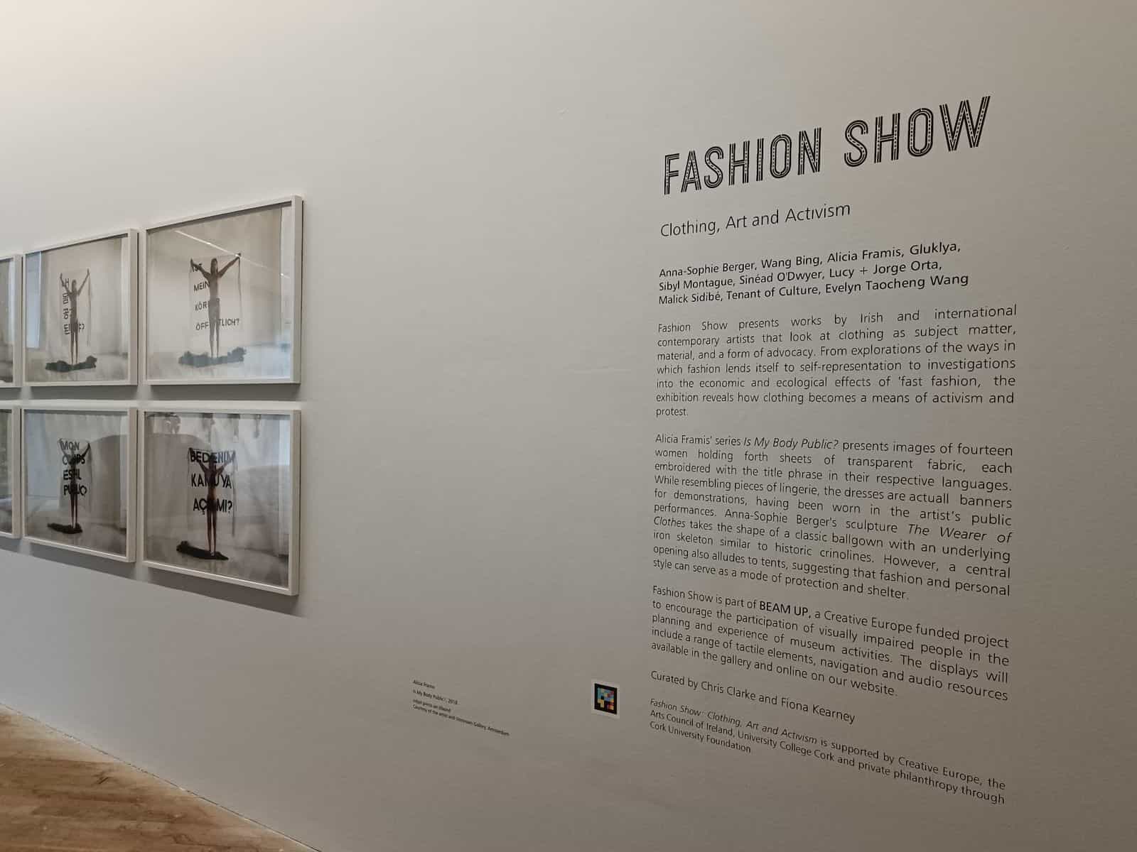 Introductory wall of “Fashion Show: Clothing, Art and Activism” at The Glucksman with a NaviLens code beside the curatorial text listing the participating artists