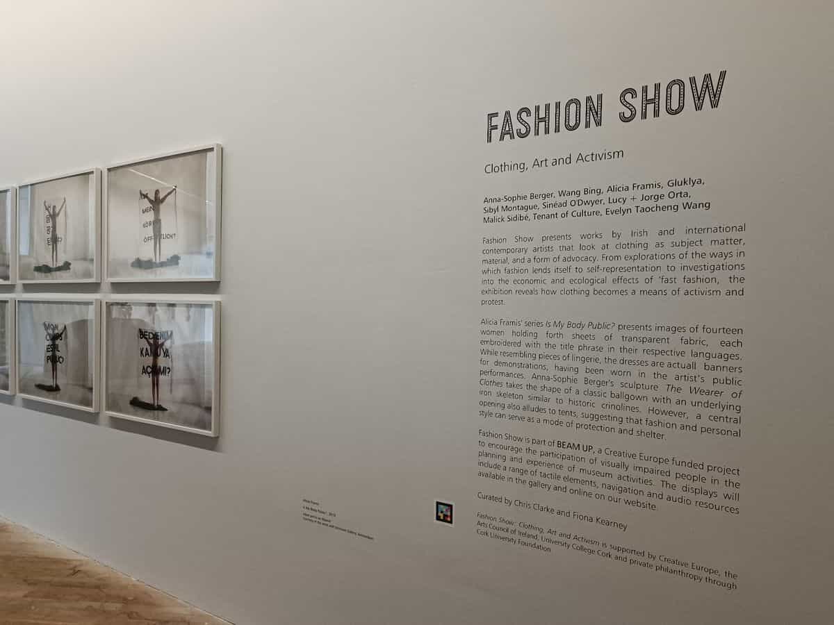 Einführungswand der Ausstellung «Fashion Show: Clothing, Art and Activism» im The Glucksman mit einem NaviLens-Code neben dem kuratorischen Text, der die teilnehmenden Künstler:innen auflistet