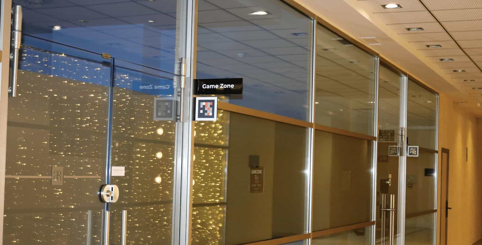 Glastüren der Game Zone des AR Diamante Beach Calpe mit schwarzem 'Game Zone'-Schild und zwei NaviLens-Codes (einer mit Markern, einer Standard) am Glas