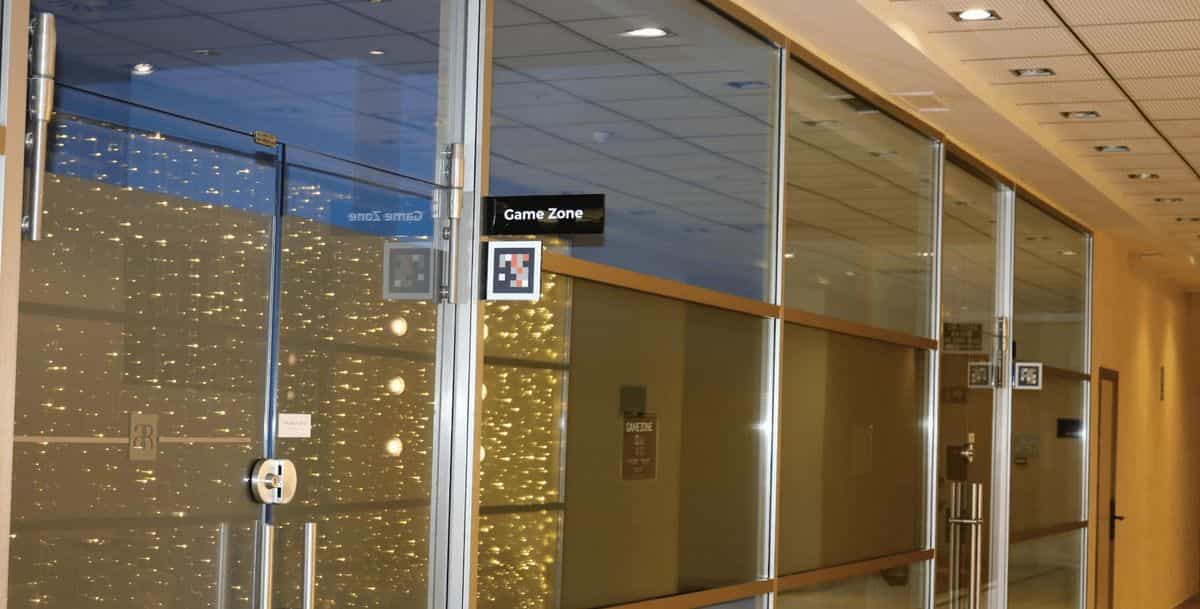 Glass doors of the Game Zone at the AR Diamante Beach Calpe with a black 'Game Zone' sign and two NaviLens codes (one with markers, one standard) on the glass