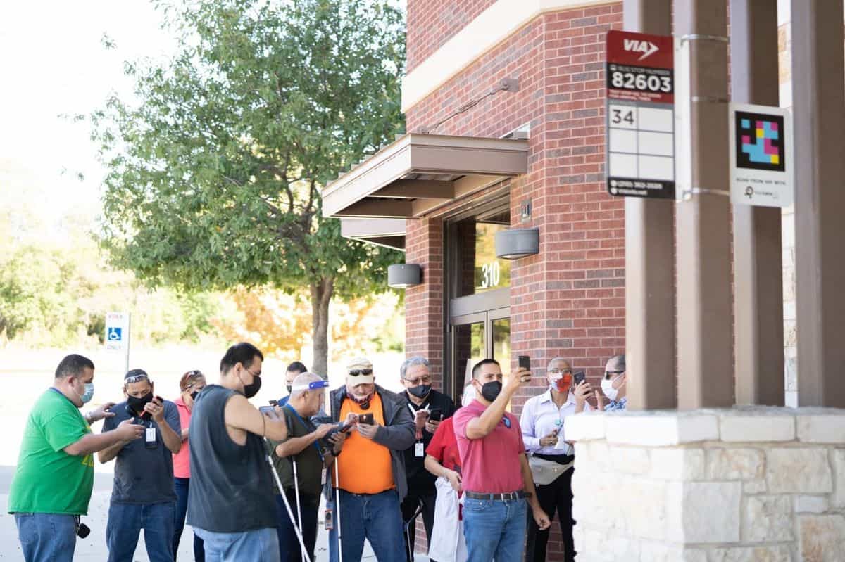 Grupo de personas, varias con bastón blanco, escanean un código NaviLens