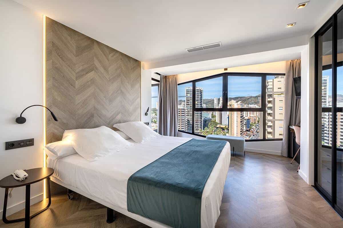 Classic double room at the Climia Belroy with two beds dressed in white, padded headboard and natural light from the terrace