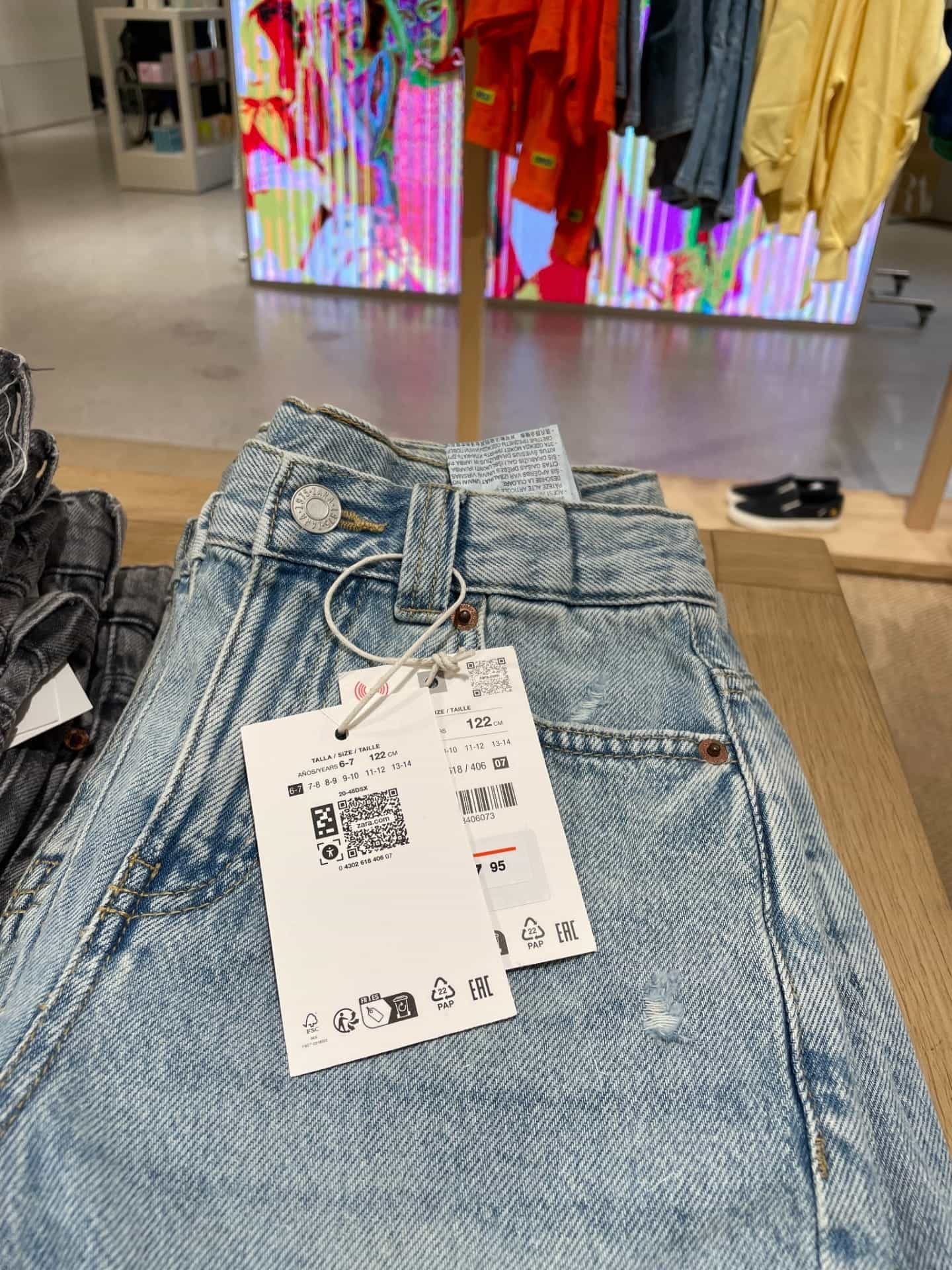Primer plano de un colgante NaviLens sujeto a unos vaqueros en un expositor de tienda.