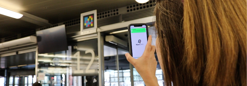 Boardingbereich von Madrid-Puerta de Atocha: Eine Reisende scannt mit ihrem Handy den NaviLens-Code über dem Zugang zu Gleis 12; die App bestätigt das Boarding für ihren Zug.