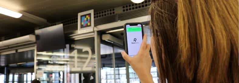 Sala d’imbarco di Madrid-Puerta de Atocha: una viaggiatrice inquadra con il telefono il codice NaviLens posto sopra la porta di accesso al binario 12 e l’app le conferma l’imbarco per il suo treno