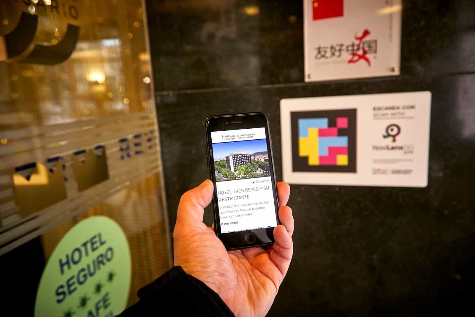 iPhone davanti alla vetrata d’ingresso dell’Hotel Tres Reyes di Pamplona con codice NaviLens