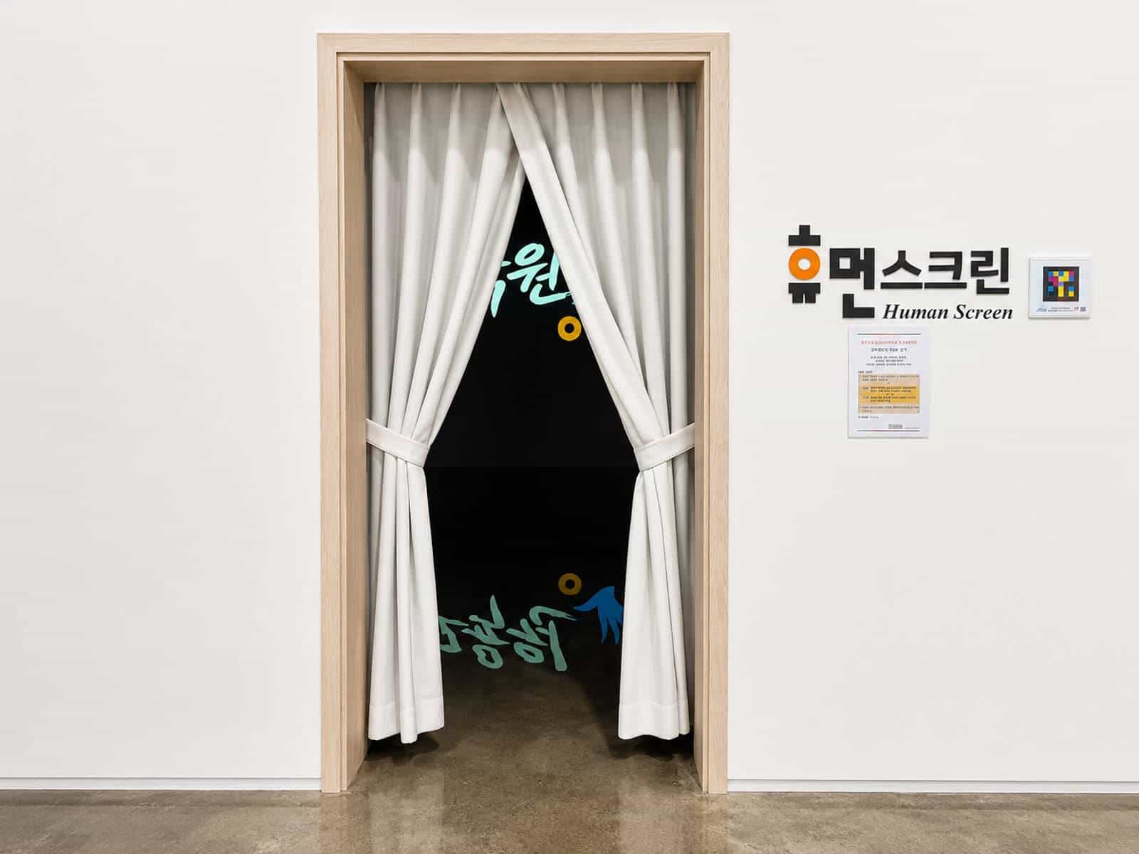 Doorway with white curtains of the “Human Screen” installation; next to the sign, a NaviLens code and the room's instructions