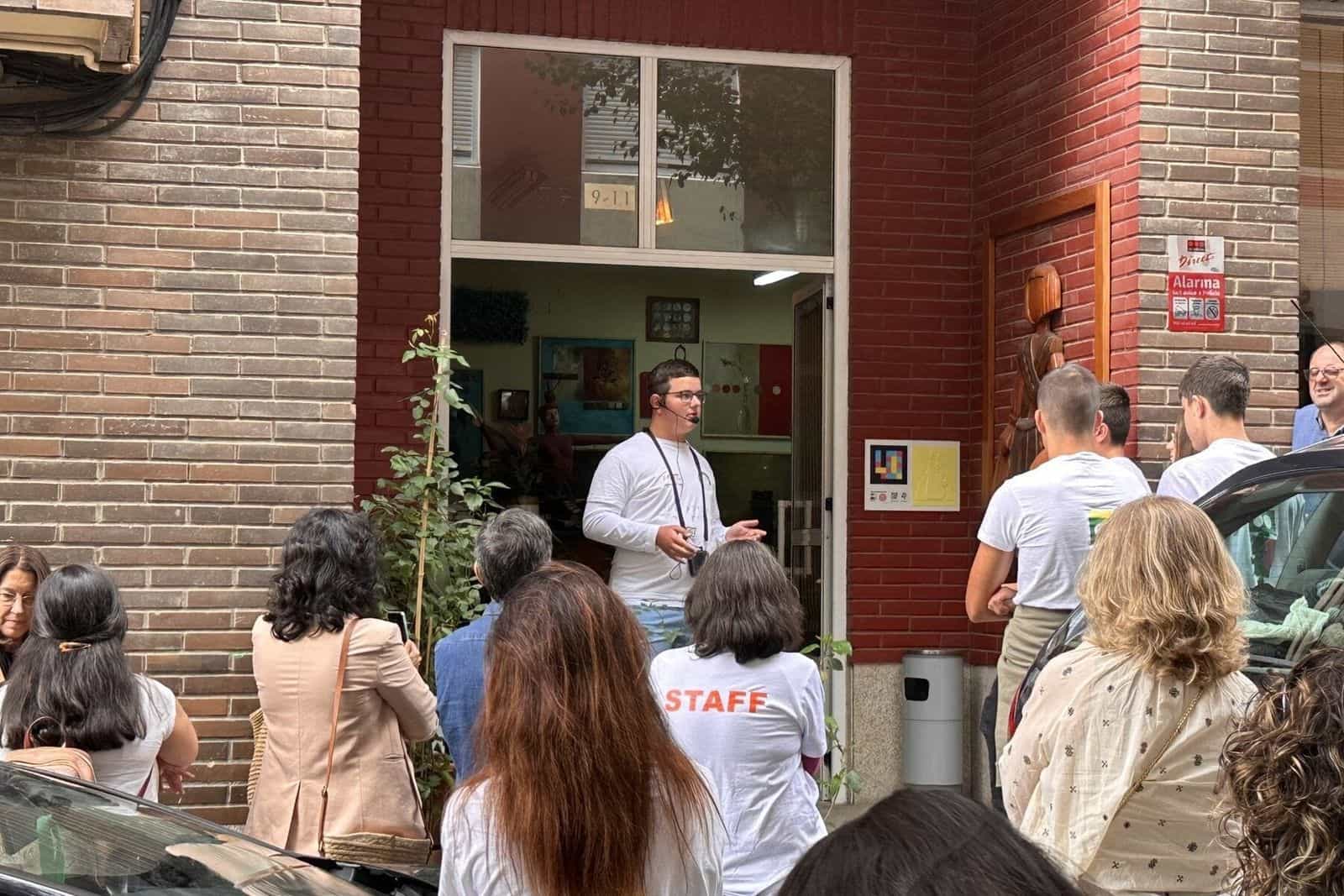 Inaugurazione del progetto a Canido: uno studente con il microfono presenta il progetto al pubblico davanti allo studio di Eduardo Hermida; sulla parete, il pannello con codice NaviLens e il rilievo giallo di una Menina