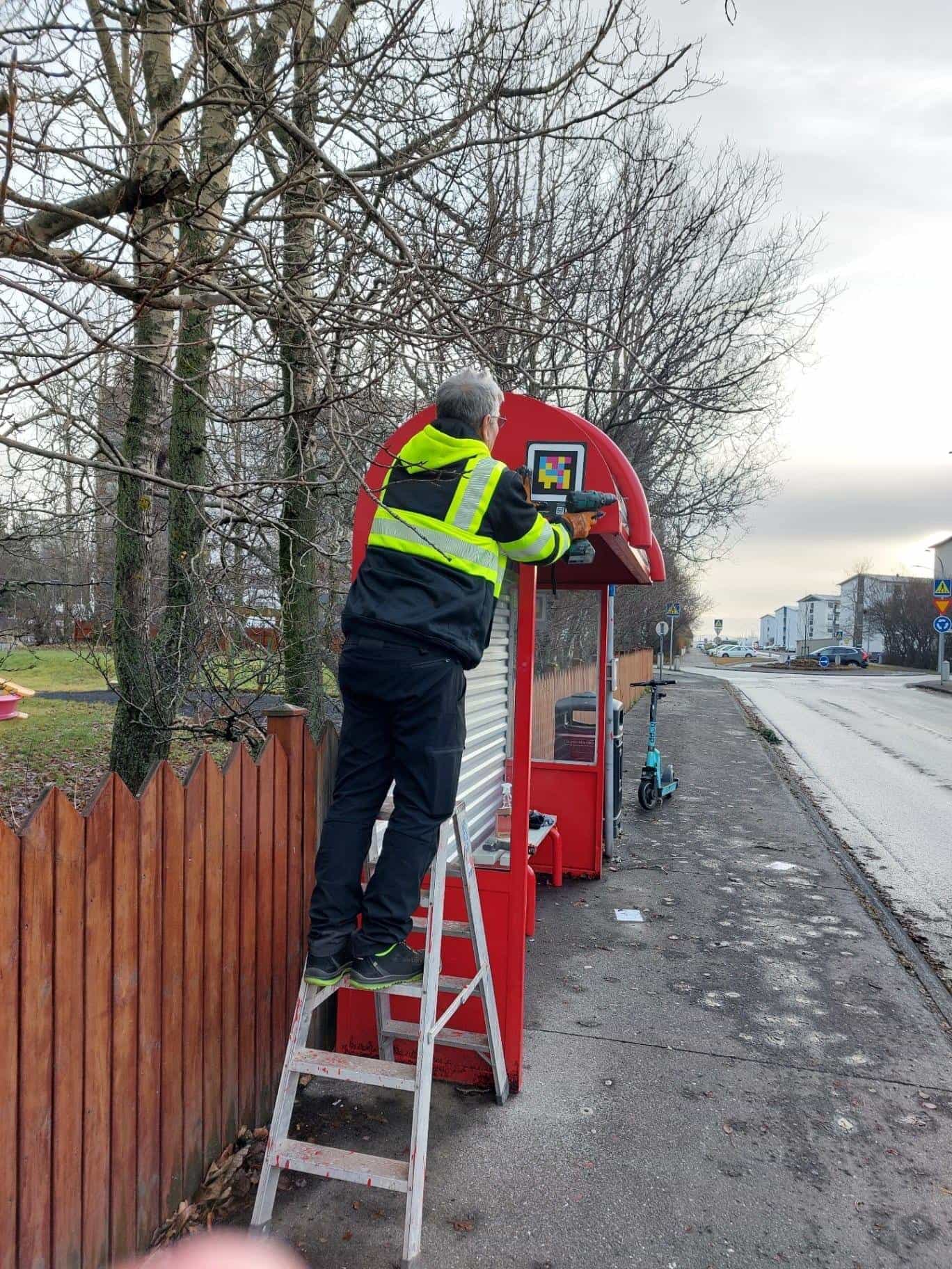 Worker drilling a NaviLens code onto the headboard of a Strætó biðstöð