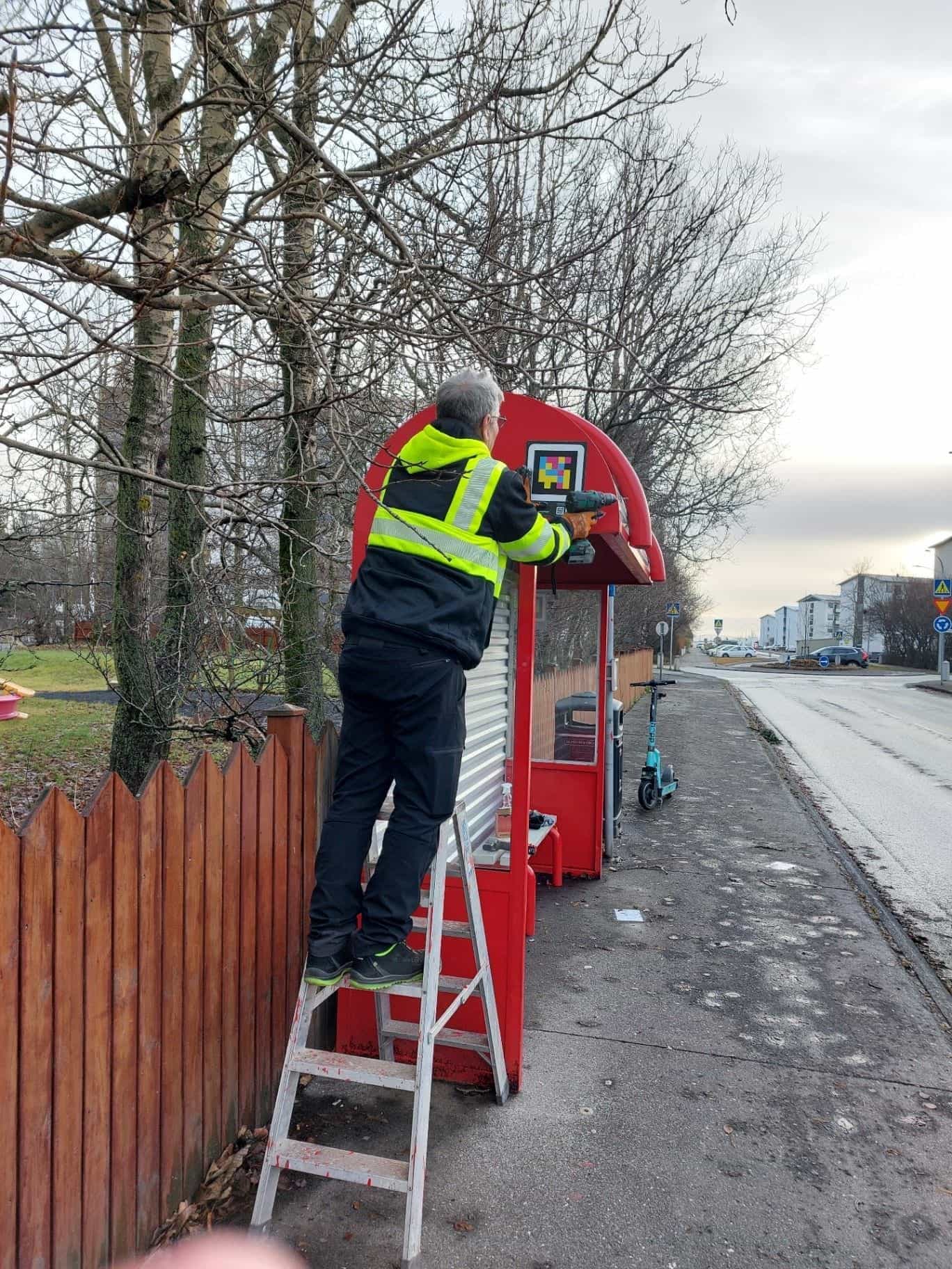 Operatore che installa con il trapano un codice NaviLens sulla testata di una biðstöð di Strætó