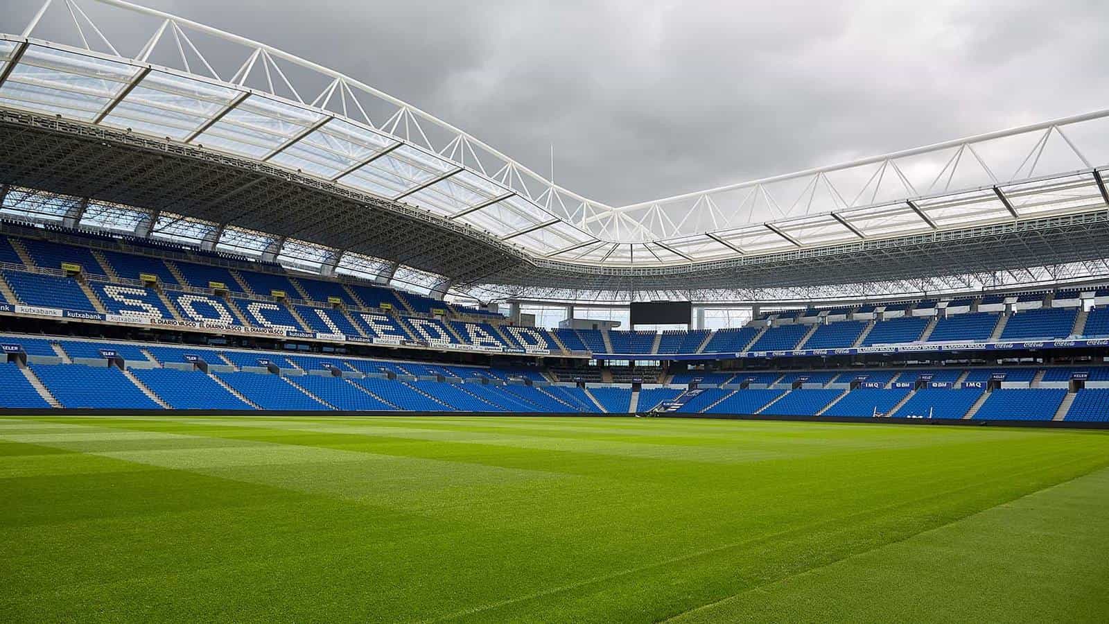 Inside Reale Arena from the pitch — blue stands spelling “SOCIEDAD” in the seats, with the translucent roof over the upper tier