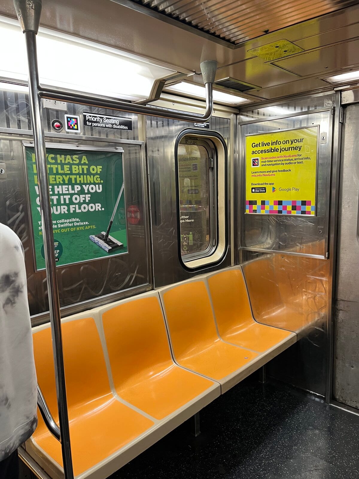 Intérieur d'une nouvelle voiture R211 avec sièges orange et panneau carré jaune MTA : «Get live info on your accessible journey. Scan codes with NaviLens for real-time service status, arrival info, and navigation by audio or text. Learn more and give feedback at mta.info/NaviLens»