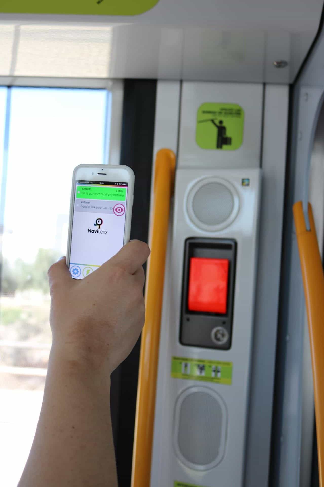 Persona che inquadra un codice NaviLens collocato in cima a una pensilina del Tranvía de Murcia, con lo schermo LED dei prossimi arrivi in fondo