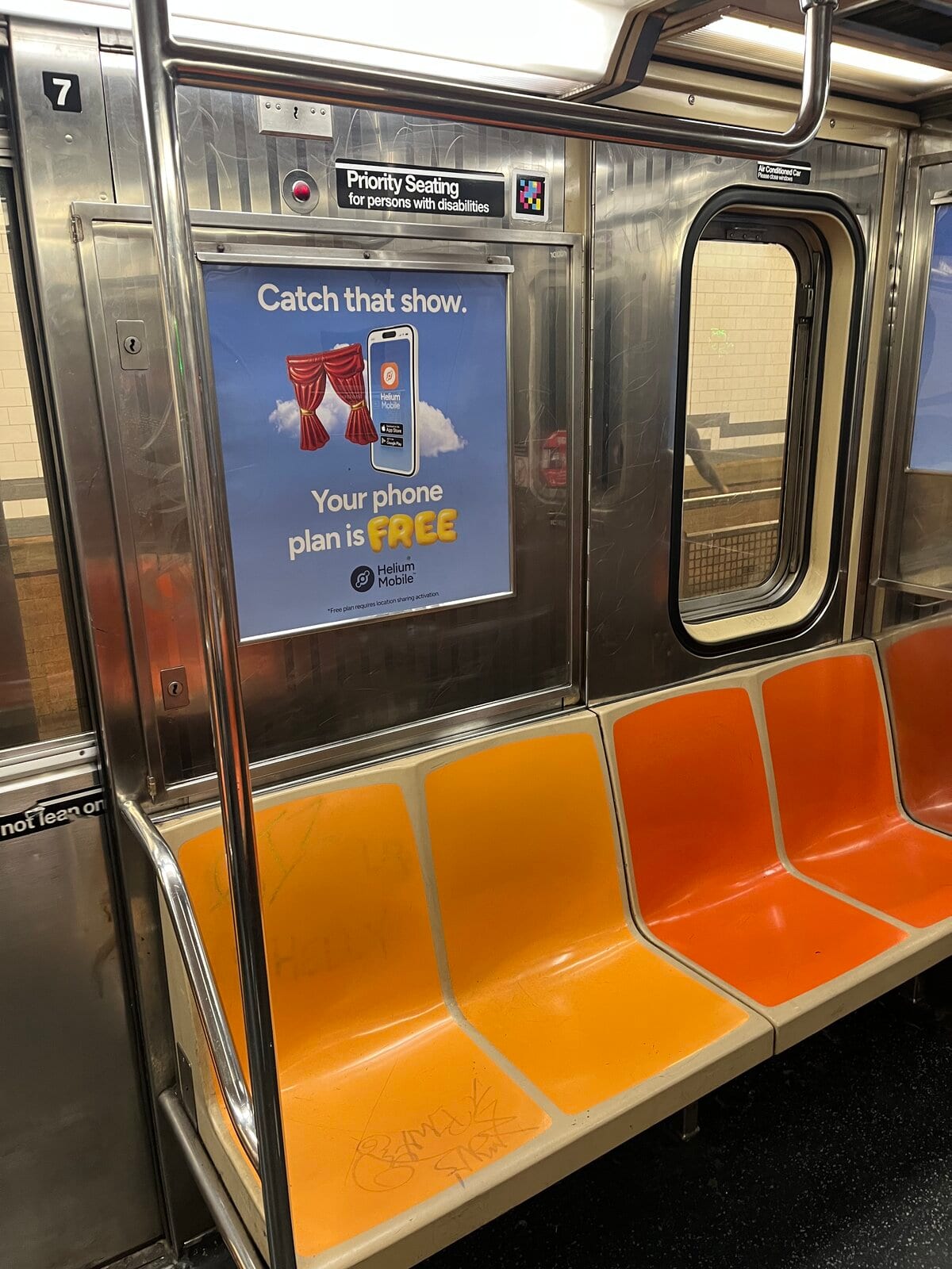 Vue large du banc orange de la voiture avec le panneau «Priority Seating for persons with disabilities» et le code NaviLens en haut, à côté de la porte et de la publicité «Catch that show. Your phone plan is FREE»