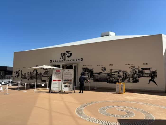 「KANSAI PAVILION」のサインと、和歌山・鳥取・徳島・福井・三重各県の文化アイコンを描いた白黒の壁画を備えた関西パビリオン外観