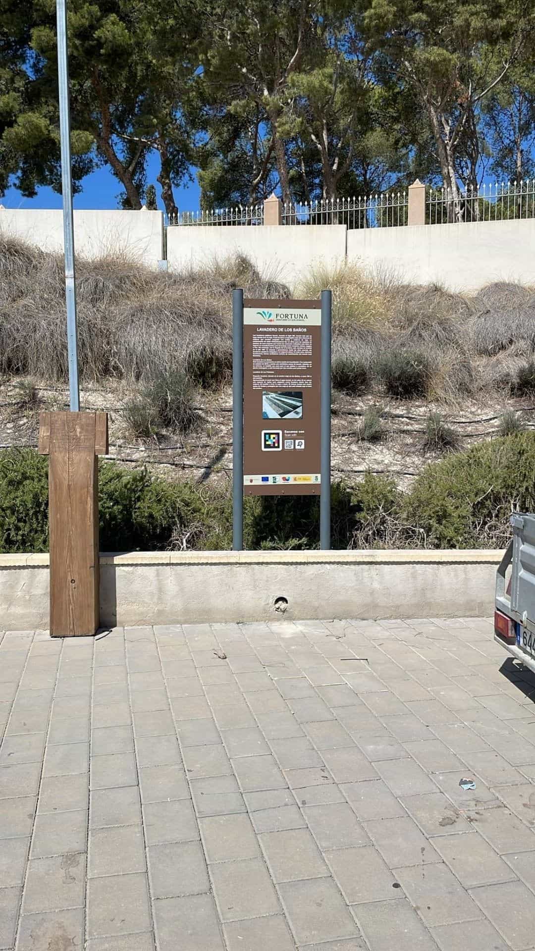 Lavadero de Los Baños de Fortuna: tótem patrimonial con fotografías del lavadero, código NaviLens y vegetación de la zona termal al fondo