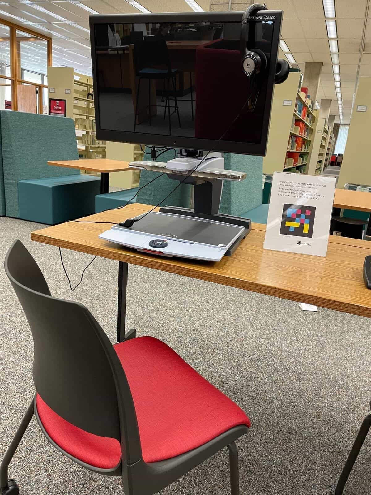 Barrierefreier Arbeitsplatz in der NIU-Bibliothek mit ClearView Speech-Monitor, Prioritätsschild für assistive Technologien und NaviLens-Code neben den Kontaktdaten von Kimberly Shotick
