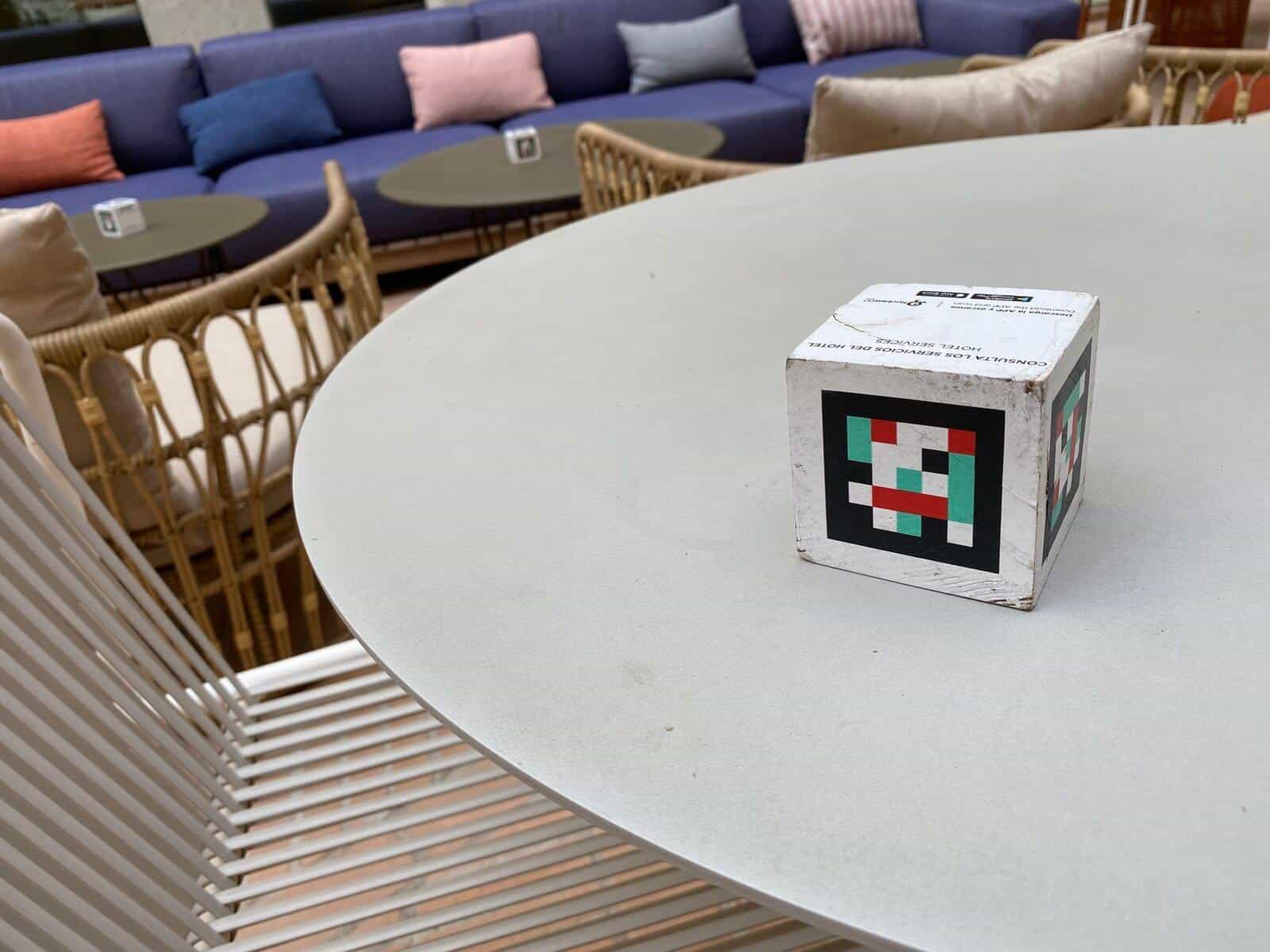 Round white lounge table at ibis Styles Sevilla with a NaviLens cube on top; large blue sofa with colourful cushions in the background