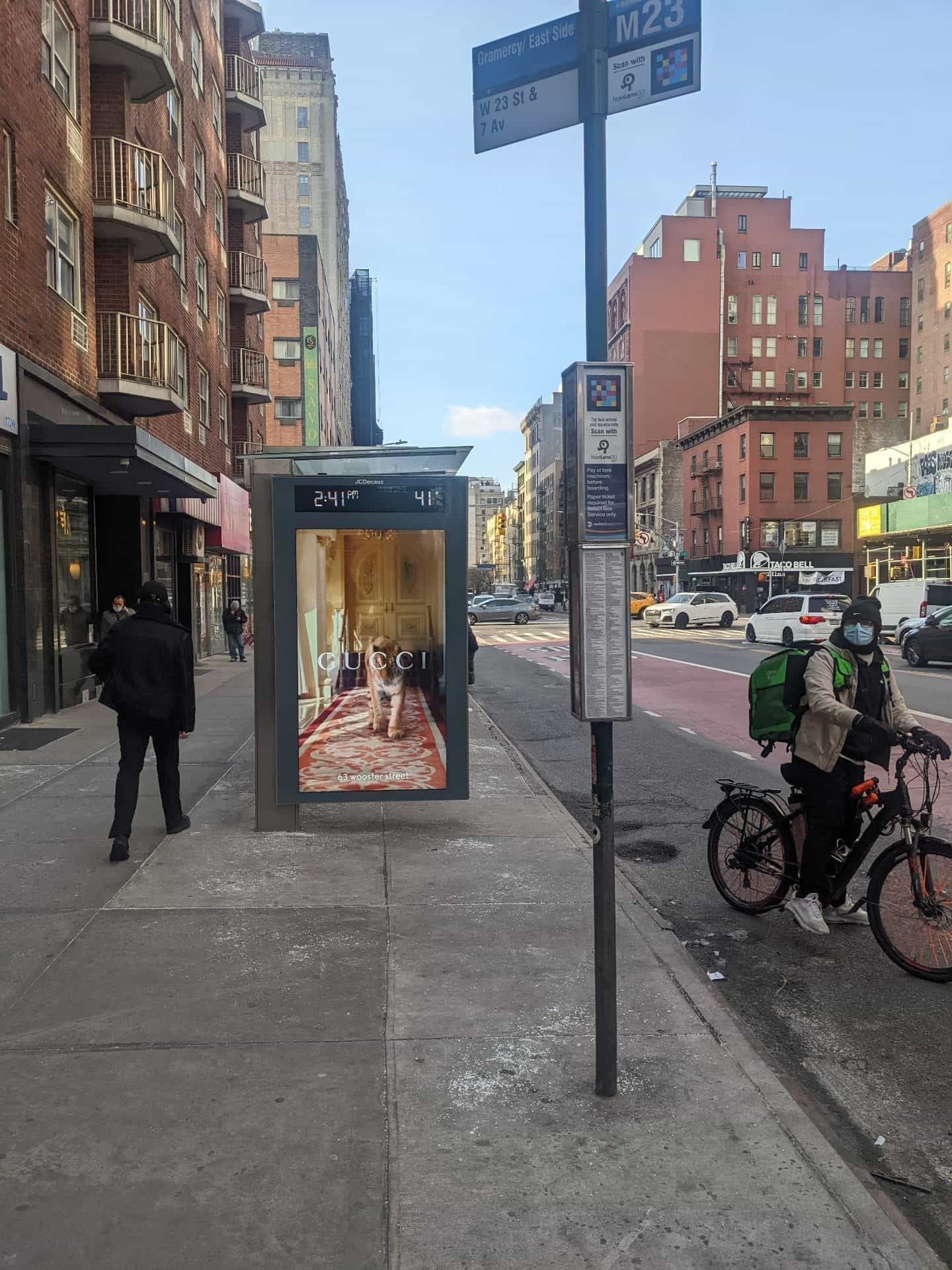 M23-Bushaltestellenpfosten «Gramercy / East Side · W 23 St & 7 Av» in Manhattan: offizielles blaues MTA-Schild mit einem NaviLens-Code in der oberen rechten Ecke und darunter ein Panel «Scan with NaviLens GO – for bus arrival and service info»