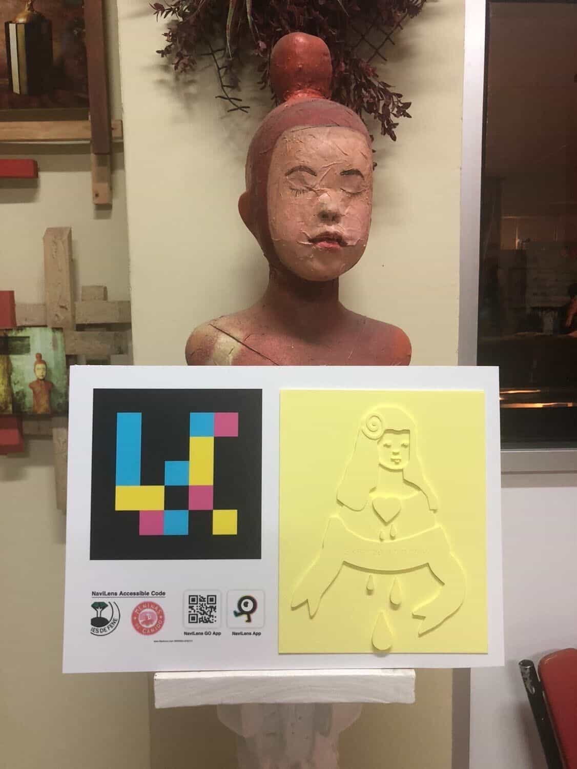 Panel del proyecto con código NaviLens y relieve amarillo de la Menina con corazón y lágrimas pintada en el mural «Sigamos bailando» de Canido