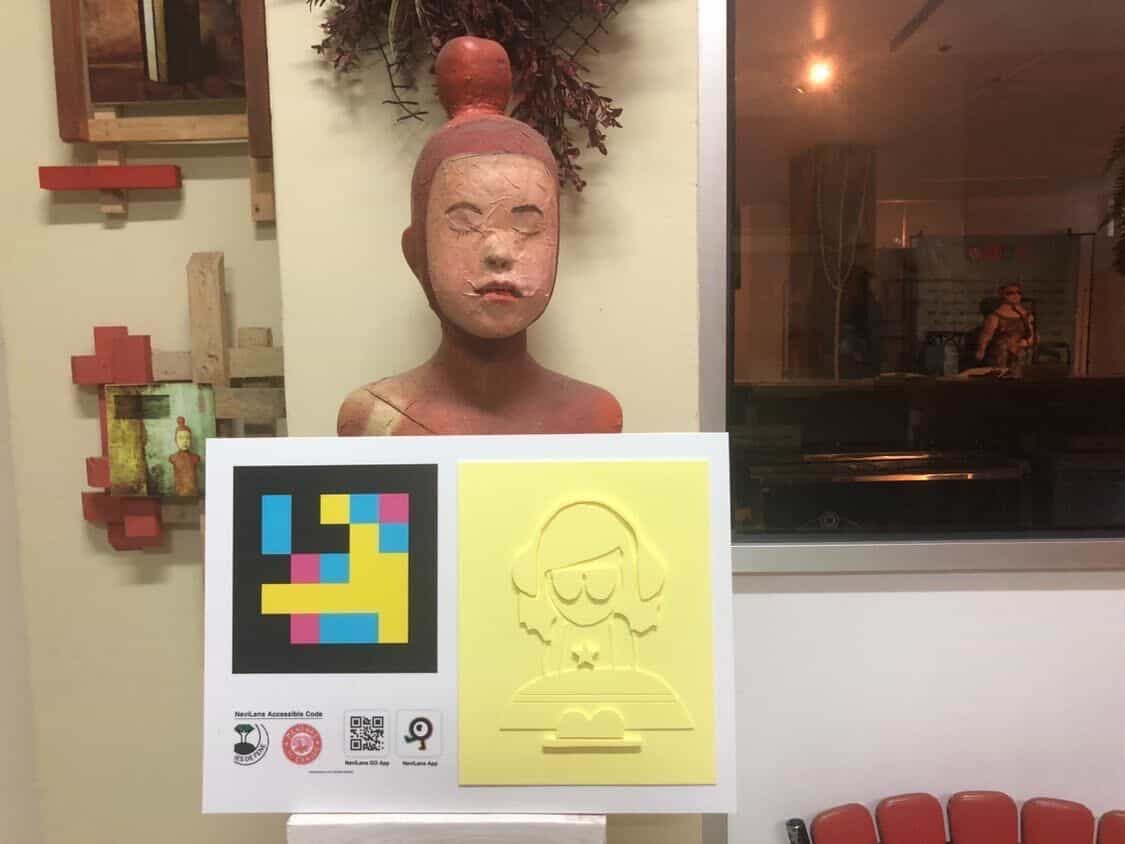 Panel del proyecto con código NaviLens y relieve amarillo de una Menina pequeña con sombrero, sostenido frente a un busto de cerámica del estudio del artista