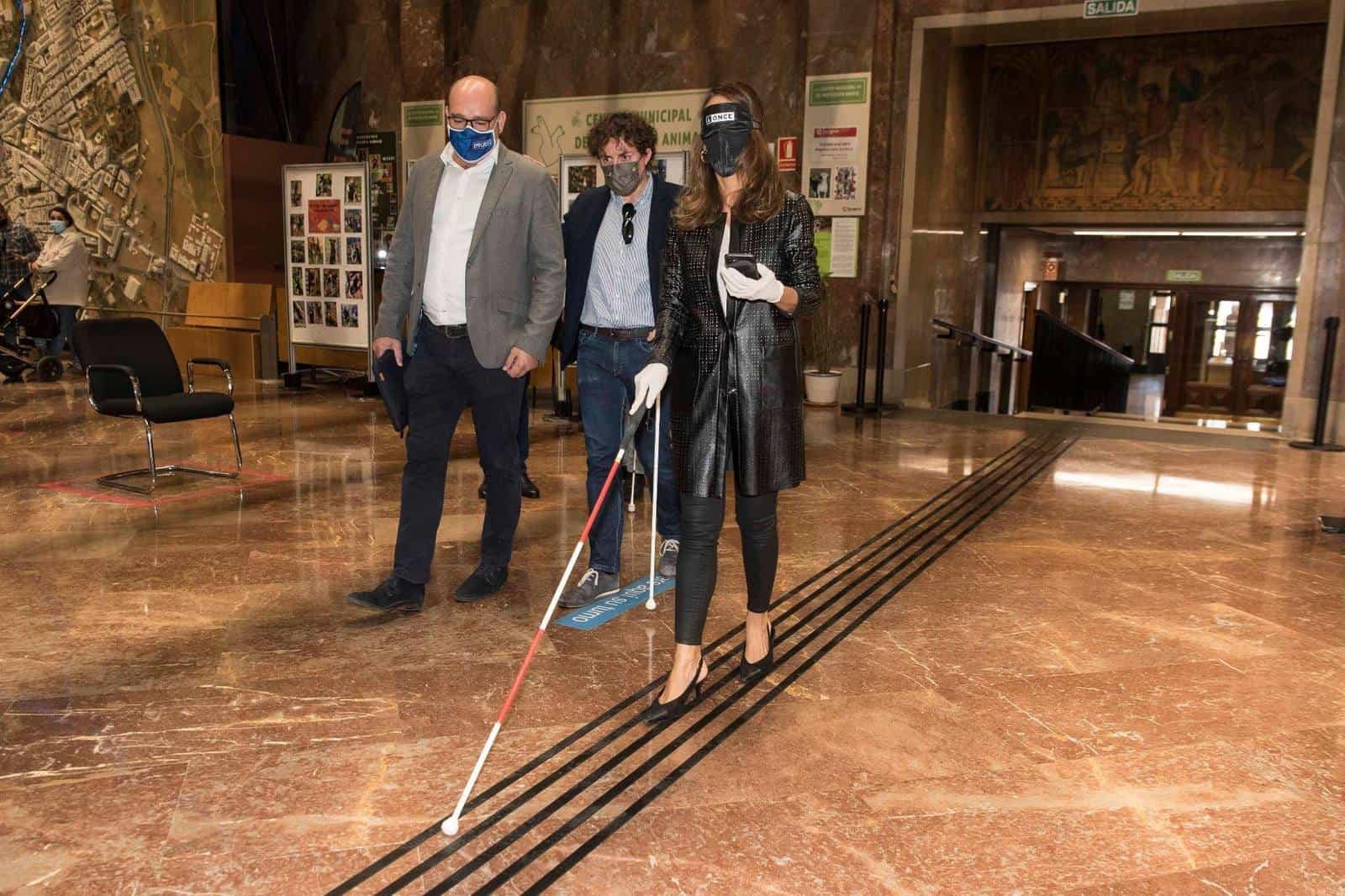 Councillor María Navarro walks with a blindfold and white cane along the tactile strip installed by Implaser on the marble floor of the Zaragoza City Council hall