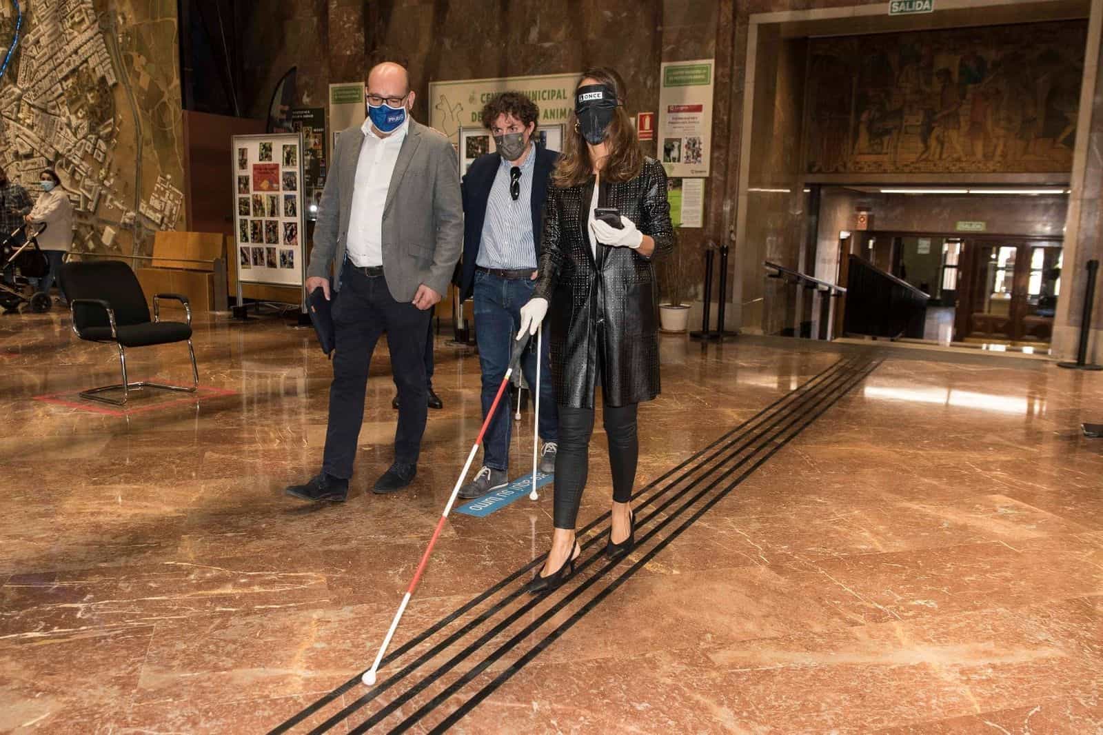 L’assessora María Navarro percorre, con mascherina oscurante e bastone bianco, la fascia tattile installata da Implaser sul pavimento in marmo della hall del Comune di Saragozza