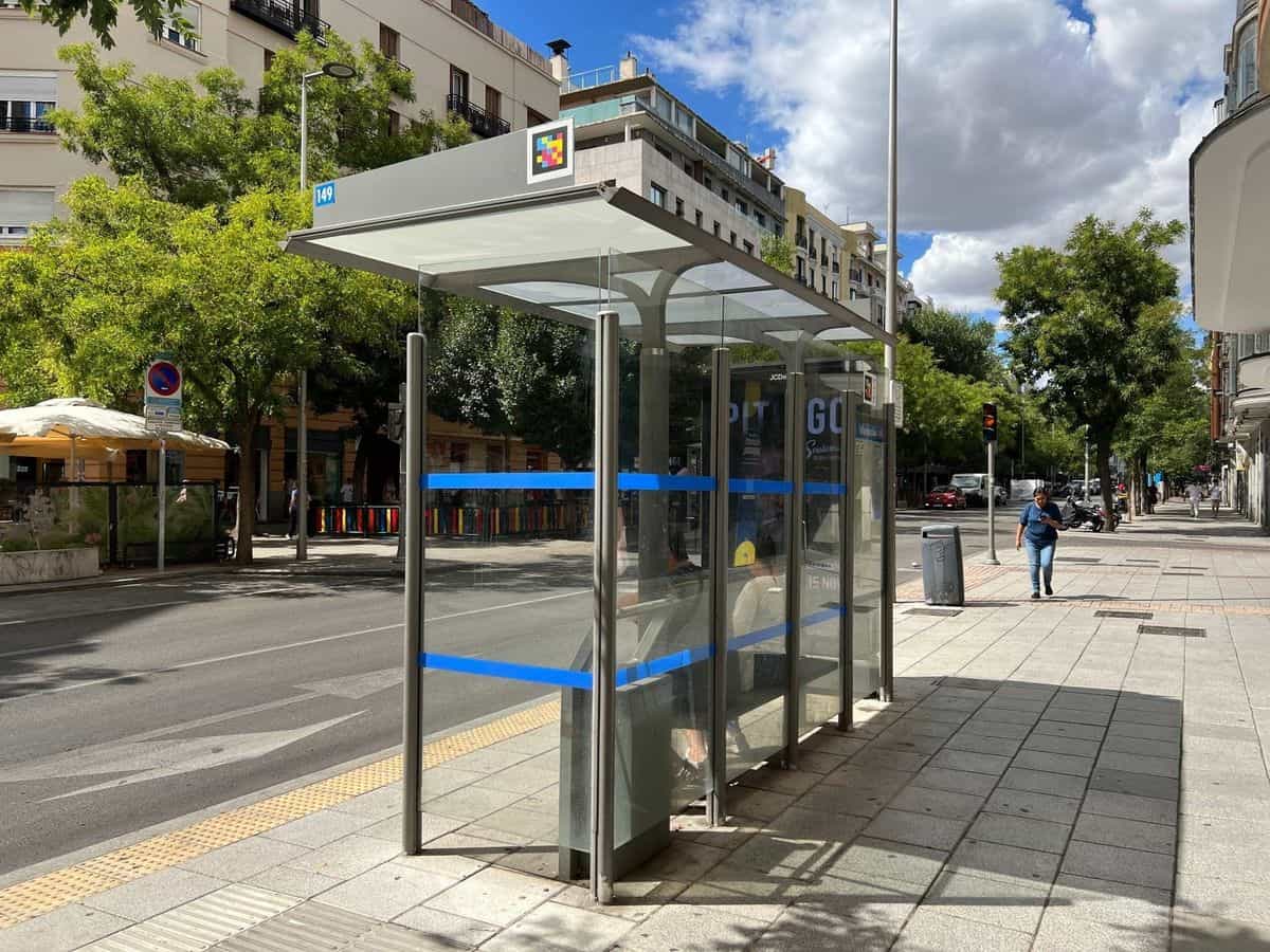 Marquesina de cristal de la EMT en la calle, con la placa numérica «149» en azul; en el frontal del techo, un código NaviLens cuadrado a colores destaca sobre fondo blanco para que la app del móvil lo detecte desde la otra acera